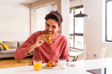 Obraz na płótnie Canvas Young mixed race man eating croissant in a kitchen on the morning