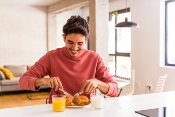 Young mixed race man eating croissant in a kitchen on the morning