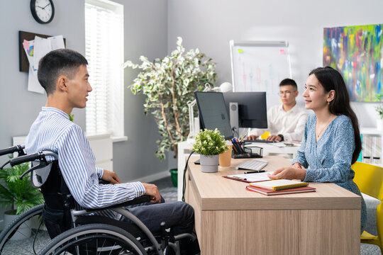 Man In Shirt Sits In Wheelchair At Desk, Opposite Him Beautiful Woman In Dress Asks Questions, They Discuss Terms Of Cooperation, Interior Of Company's Office Job Interview Customer Service