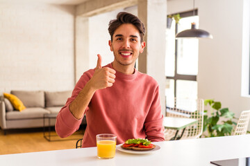 Fototapeta na wymiar Young mixed race man having breakfast in his kitchen smiling and raising thumb up