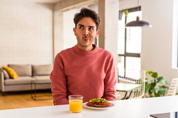 Fototapeta na wymiar Young mixed race man having breakfast in his kitchen confused, feels doubtful and unsure.