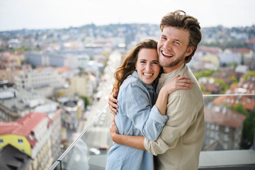 Happy young couple in love looking at camera outdoors on balcony at home, hugging.