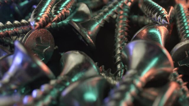 Self-cutting screws with a special external thread are scattered on a dark surface. Reflection of light on a shiny surface. Materials for repair. High quality. 4k footage.