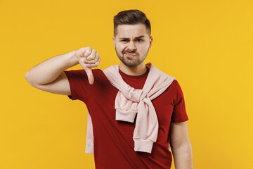 Young disappointed displeased sad man 20s wear red t-shirt casual clothes showing thumb down...