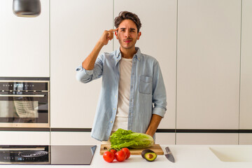 Young mixed race man preparing a salad for lunch pointing temple with finger, thinking, focused on a task.