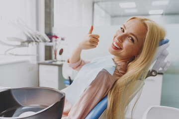 Close up young smiling happy calm woman covered by napkin show thumb up gesture sit at dental...