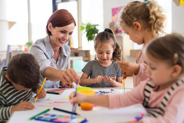 Obraz na płótnie Canvas Group of small nursery school children with teacher indoors in classroom, painting.