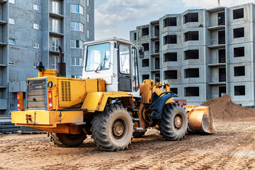 Heavy wheel loader with a bucket at a construction site. Equipment for earthworks, transportation and loading of bulk materials - earth, sand, crushed stone.
