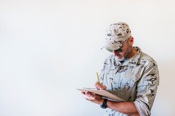 Caucasian man in camouflaged military uniform writing in notebook.