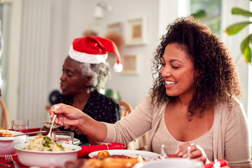 Multi Generation Family In Paper Hats Enjoying Eating Christmas Meal At Home Together