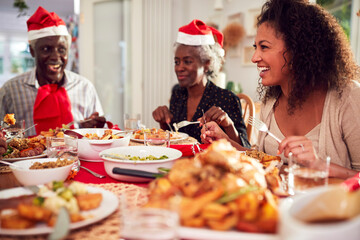 Multi Generation Family In Paper Hats Enjoying Eating Christmas Meal At Home Together
