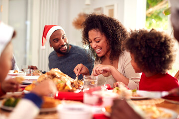 Family In Paper Hats Enjoying Eating Christmas Meal At Home Together