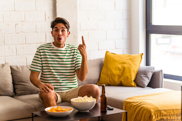 Young mixed race man eating popcorns sitting on the sofa having some great idea, concept of creativity.
