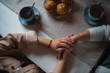 Fototapeta na wymiar Top view of senior mother having coffee with adult daughter indoors at home, holding hands.