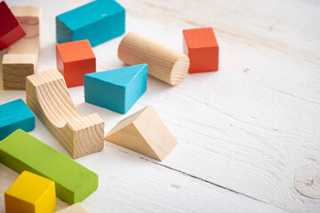 Multi-colored wooden cubes made of natural wood are scattered on a white wooden table. Learning and education concept.