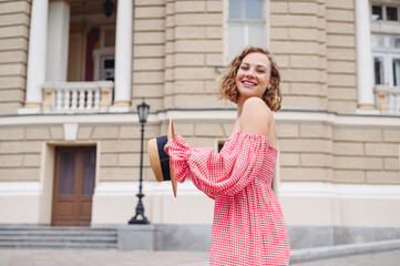 Side view young beautiful smiling happy blonde woman in pink off-the-shoulder dress hat walk in city center standing outdoor near old building People urban summer time lifestyle architecture concept