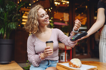 Young woman in casual clothes at cafe buy breakfast sit at table hold wireless bank payment...