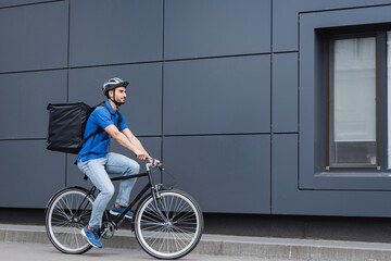 Arabian deliveryman with backpack riding bike on urban street