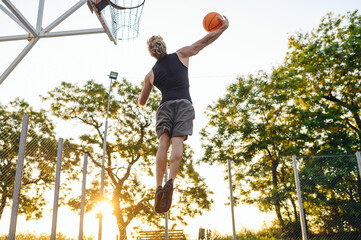 Young side view strong sportsman man in sports clothes training shooting free throw fly high jump scoring basket playing with ball at basketball game playground court Outdoor courtyard sport concept