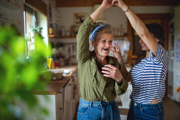 Happy senior mother having fun with adult daughter indoors at home, dancing.