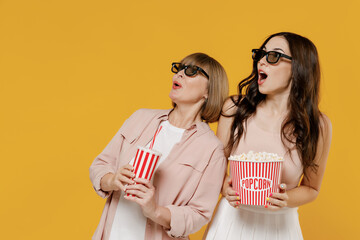Two young amazed daughter mother woman in 3d glasses watch movie film hold bucket of popcorn cup of...