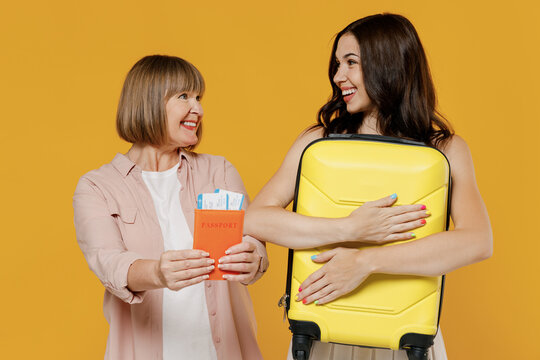 Traveler tourist fun two women in casual clothes hold passaport ticket suitcase isolated on plain yellow color background studio. Passenger travel abroad weekends getaway. Air flight journey concept.