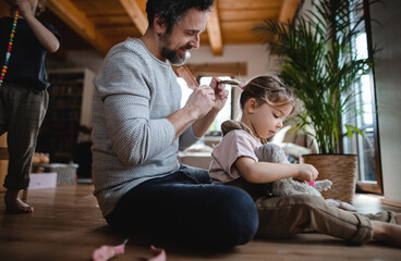 Mature father with small son and daugther resting indoors at home, playing and combing hair.