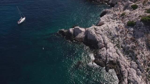 Sailboats Near Rugged Coastline On Bay Of The Island Ratonneau, Frioul Archipelago, Southern France. - Aerial Pullback