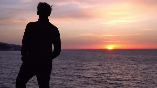 Sad young alone man looks thoughtfully at the ocean. Beautiful sunrise background. Travel and self-isolation, social distancing. Nature, sea, beach, morning