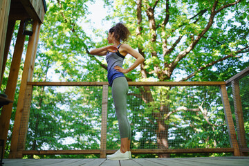 Happy mid adult woman doing exercise outdoors on terrace of tree house, weekend away and digital detox concept.