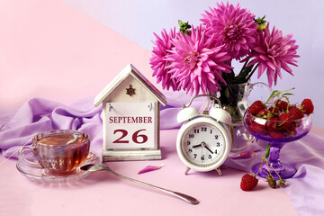 Calendar for September 26 : the name of the month in English, cubes with the number 26, a bouquet of pastel dahlias, raspberries in a cup, an alarm clock, a cup of fragrant tea