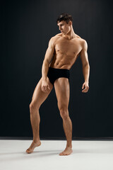 Fototapeta na wymiar sporty man with muscular body in black panties posing against a dark background
