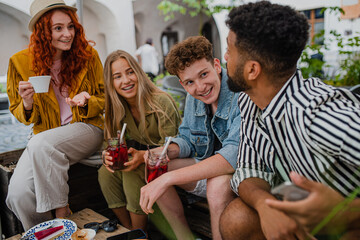 Group of happy young people sitting in outdoors cafe on town trip, talking.