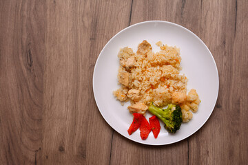 Plate of rice and meat pilaf with pieces of vegetables. On a wooden surface, top view.