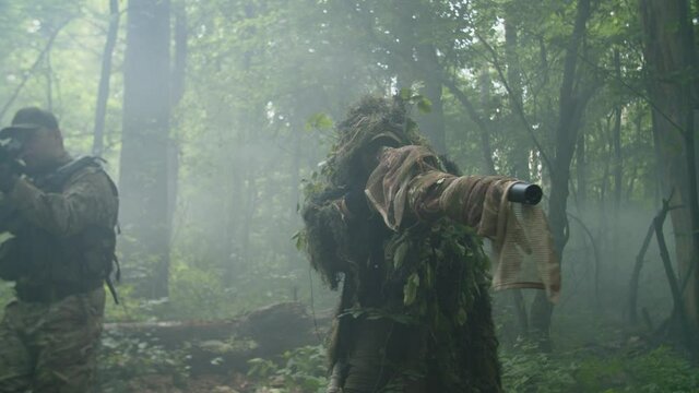 Front view of counter-terrorist special forces group in combat gear, weapon in firing position, wading through thicket of dense forest in fog. Military group conducting reconnaissance in force