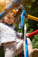 Cute toddler girl having fun on playground. Happy healthy little child climbing on different equipment.