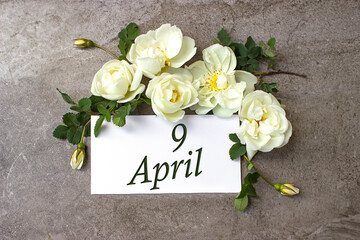 April 9th. Day 9 of month, Calendar date. White roses border on pastel grey background with...