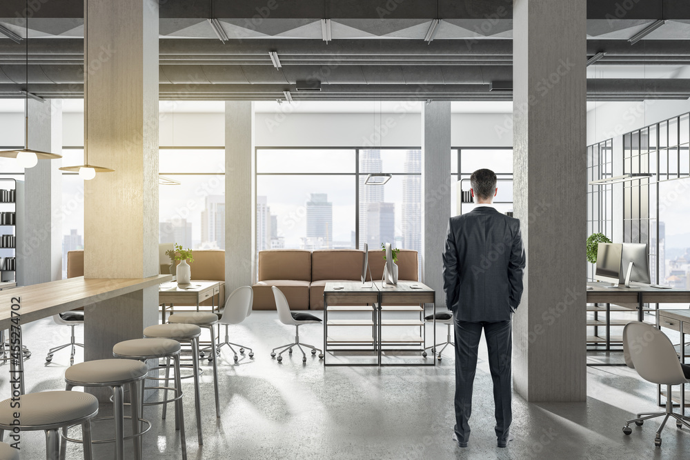 Poster businessman standing in modern coworking office interior with bright city view and concrete flooring