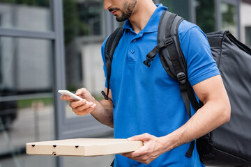 Cropped view of deliveryman holding pizza box and smartphone outdoors