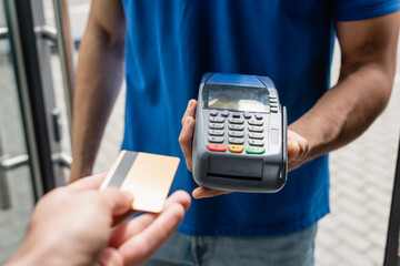 Cropped view of man holding credit card near courier with payment terminal