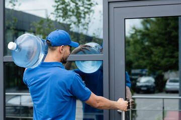Muslim deliveryman holding bottle of water while opening door of building