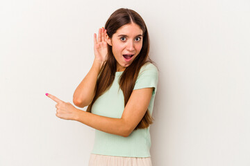 Young caucasian woman isolated on white background trying to listening a gossip.