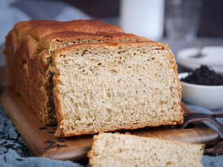 Close up of a loaf of soft fluffy organic bread bun earl grey tea perfume and its leaf in bread layers, with slice pieces on a wooden board. Tea leaves in background 
