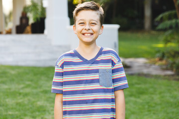 Portrait of smiling caucasian boy outside house looking at camera in garden