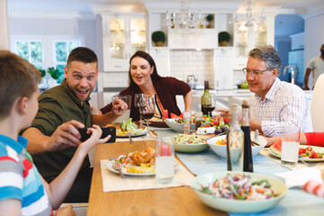 Caucasian grandfather and parents with daughter and son showing phone while having dinner