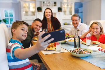 Fototapeta premium Caucasian grandfather and parents with daughter and son taking selfie while having dinner