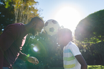 African american father with son having fun playing with football held between their heads in garden