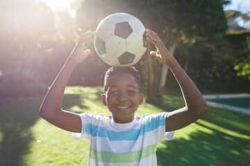 Portrait of smiling african american boy having fun and playing with football in garden