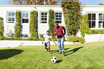 African american father with son having fun and playing football in garden