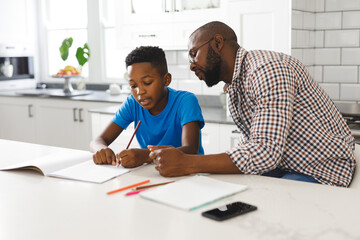 African american father and son in kitchen, doing homework together